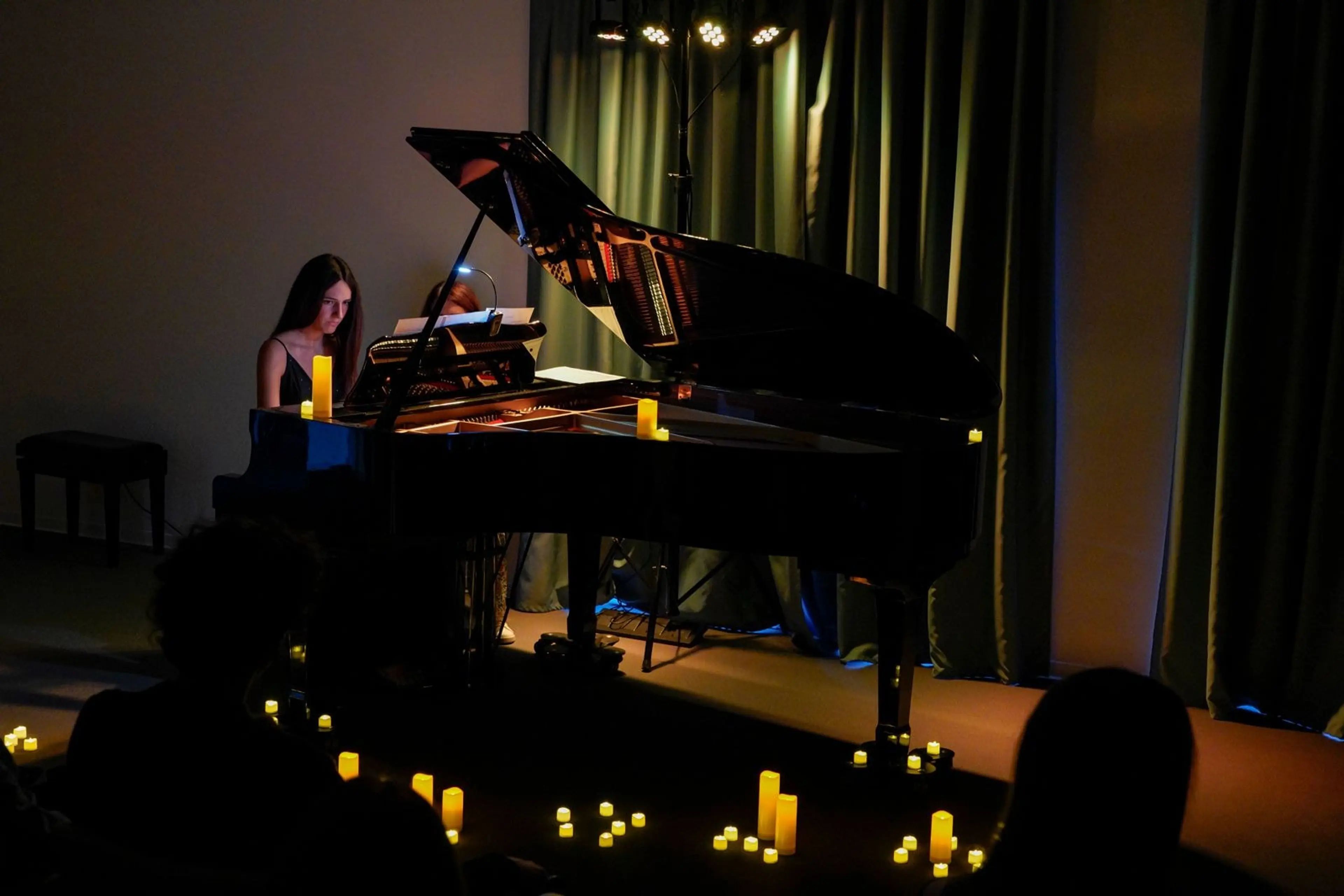 Una pianista al pianoforte a coda durante un concerto, con il palco illuminato da candele